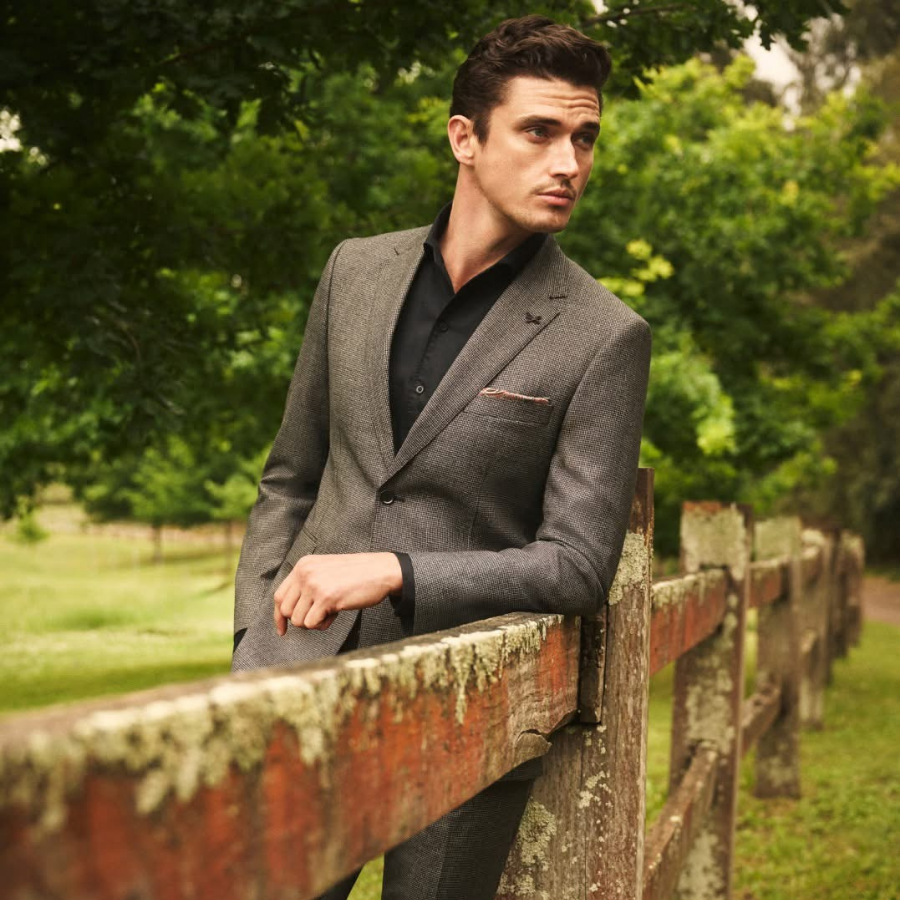 Man leaning on a fence wearing a Suits on Wall Street suit and shirt
